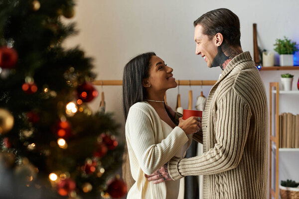 Любящая пара обнимает друг друга, празднуя Рождество дома, делясь радостью и теплотой.