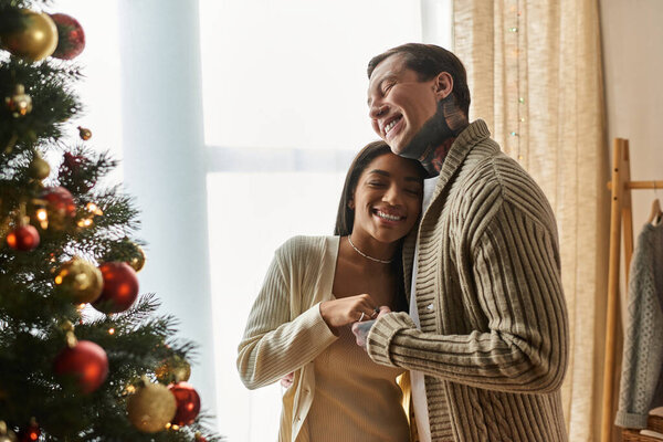 A couple shares a cozy, joyful moment by their beautifully decorated Christmas tree.