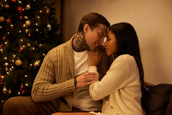 Пара наслаждается друг с другом компанией рядом с красиво освещенной елкой вместе.