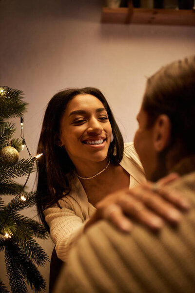 Пара наслаждается друг с другом компанией, в окружении праздничных украшений и елки.