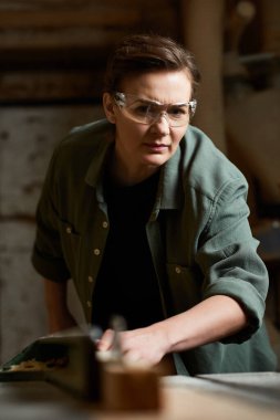 A focused female carpenter engages with wood, demonstrating precision and craftsmanship in her workshop. clipart