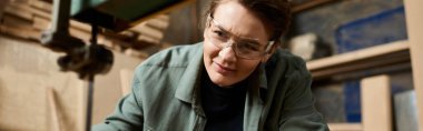 A focused female carpenter carefully shapes wood in a well-equipped workshop filled with tools and materials. clipart