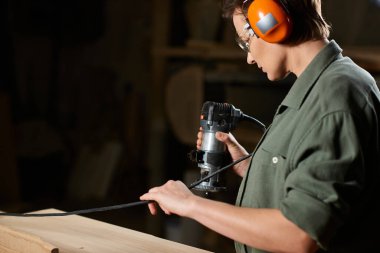 A focused carpenter operates a router while shaping wood in a well-equipped workshop, immersed in craftsmanship. clipart