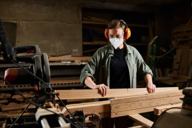 A focused carpenter works diligently with wooden planks in a well-equipped workshop, demonstrating craftsmanship. clipart