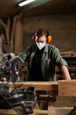 A dedicated female carpenter is using a saw to shape wood, surrounded by tools in a lively workshop. clipart