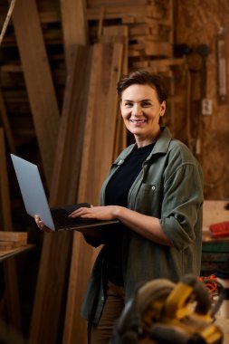 A skilled carpenter uses a laptop in her workshop, blending tradition with modern technology. clipart