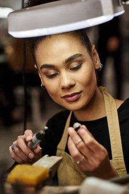 A talented woman carefully examines a jewel while working in a jewelry workshop clipart