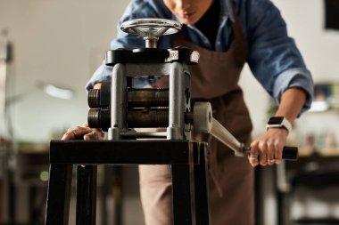 A focused craftsperson carefully rolls metal through a press, creating intricate jewelry pieces. clipart