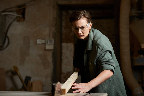 A female carpenter expertly shapes wood while focused in her workshop, surrounded by tools and materials.