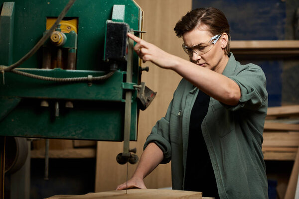 A talented female carpenter focuses on her task as she expertly operates a powerful saw in the workshop.