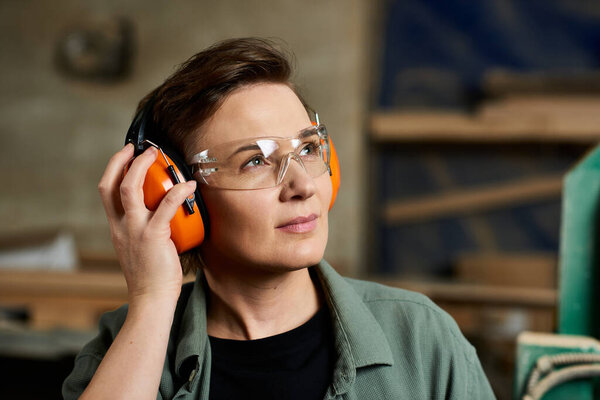 A skilled carpenter in a workshop pauses, wearing protective ear muffs and safety glasses, ready to create.