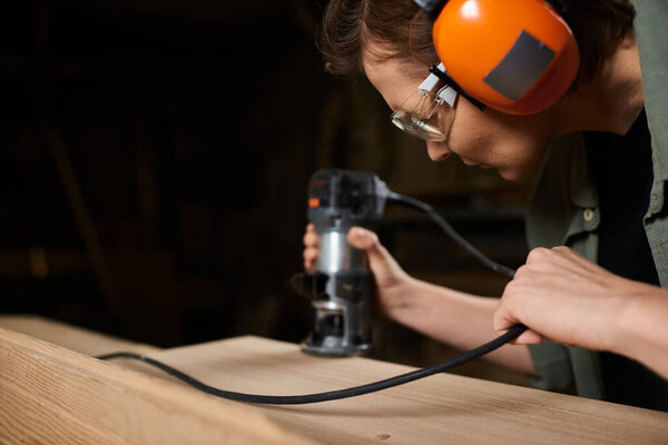 A dedicated carpenter shapes wood meticulously in her workshop, showcasing craftsmanship and focus.