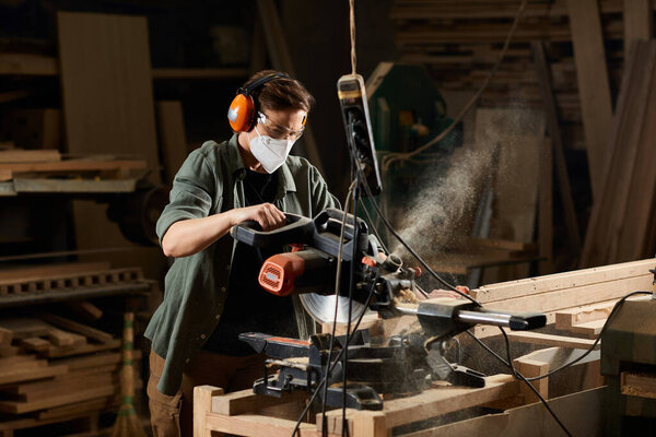 In a bustling workshop, a skilled female carpenter diligently works with a power saw to shape wooden pieces.