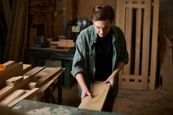 A talented woman meticulously shapes wood in her workshop, showcasing her craftsmanship and focus.