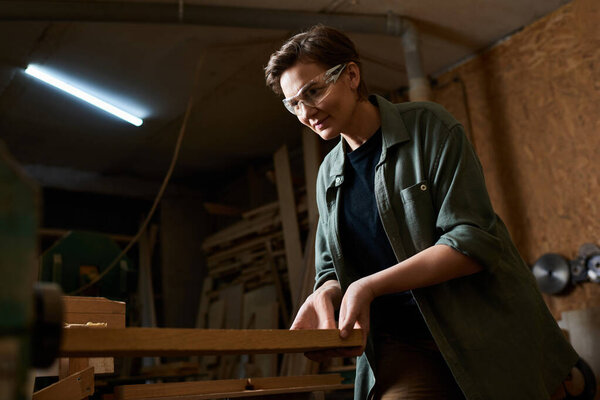 A talented female carpenter meticulously works with wood in her well-equipped workshop, showcasing craftsmanship.