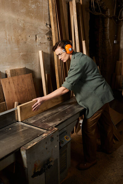 A skilled female carpenter carefully works on wood, showcasing craftsmanship in her workshop filled with materials.