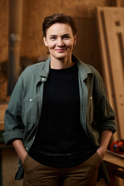 A talented carpenter stands confidently in her workshop, showcasing her dedication to woodworking and craftsmanship.