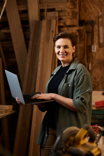A skilled carpenter uses a laptop in her workshop, blending tradition with modern technology.