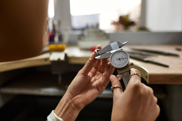 An artisan carefully measures jewels with precision tools in a bright workshop.