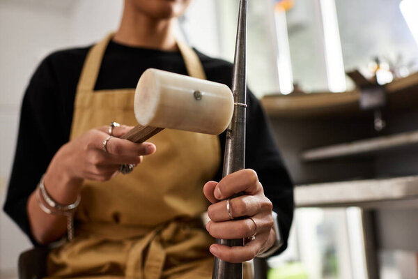 An artisan meticulously shapes metal with a wooden mallet while showcasing exquisite jewelry.