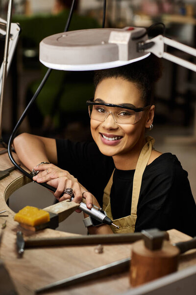 A skilled jewelry maker smiles brightly as she masterfully works with tools in her workspace.