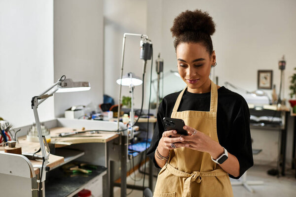 A skilled woman in an apron uses her smartphone in her artistic, tool filled workspace.