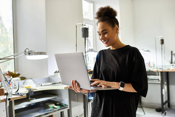 A woman smiles while typing on her laptop in a bright, art filled workspace.