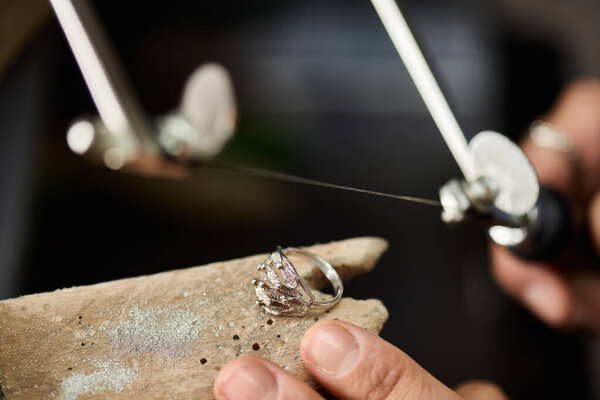 A skilled artisan works meticulously with a delicate silver ring, showcasing craftsmanship.