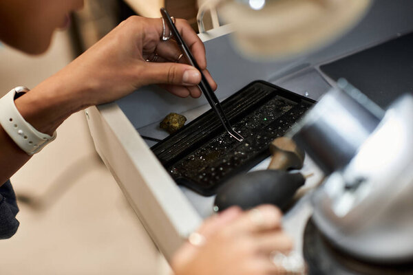 A skilled artisan carefully examines sparkling jewels with precision tools in a bright workspace.