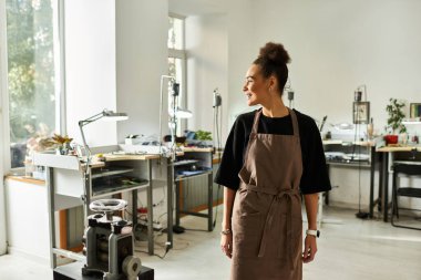 Yetenekli bir kadın, sanatsal aletler ve hazinelerle süslenmiş güneşli bir stüdyoda çalışırken gülümser..