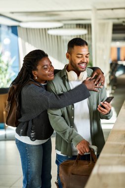Genç bir Afrikalı Amerikalı çift otel lobisinde sarılıp, heyecanlı bir şekilde tatil programlarını tartışıyor..