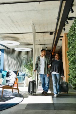 Genç bir çift, tatil maceralarına hazır modern bir otel lobisinde neşeyle geziniyor..