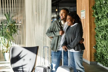 Neşeli genç bir Afrikalı Amerikalı çift birlikte gülümsüyor, canlı bir otel lobisinde anılar yaratıyor..