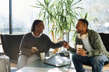 A young couple shares laughter and connection in a vibrant hotel lobby while gearing up for their vacation. clipart