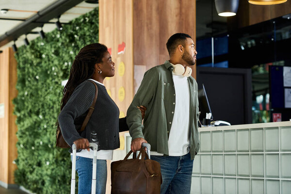 A young African American couple stands at the hotel reception, excitedly beginning their vacation journey.
