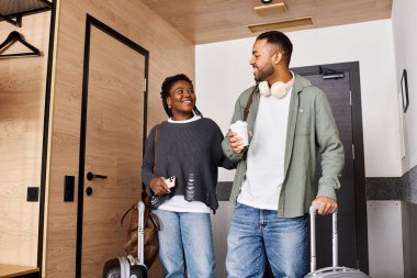 A happy couple shares laughter and drinks in their hotel room, embracing their time together on vacation. clipart