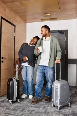 Genç bir çift, rahat bir otel odasında gülücükler ve kahkahalar paylaşıyor. Tatil kaçamaklarının tadını çıkarıyorlar..