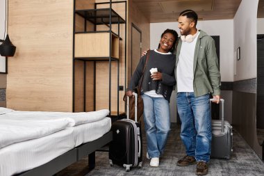 A joyful young couple shares a moment of love and relaxation in their trendy hotel room during vacation. clipart