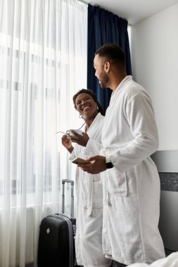 Neşeli genç bir çift, otel odalarında gülüşlerini paylaşıyor. Tatil kaçamakları sırasında birbirlerine sarılıyorlar..