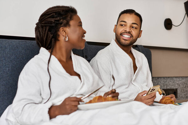 A joyful young couple shares a delightful breakfast in their hotel room, enjoying each others company.