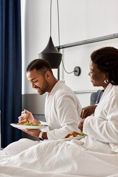 A young couple shares laughter and love while enjoying a cozy meal in their hotel room.
