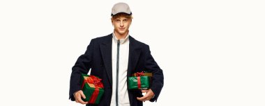 A man dressed in trendy holiday fashion holds two beautifully wrapped Christmas gifts, showcasing festive joy. clipart