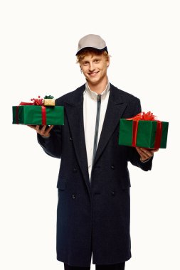 Şık bir tatil kıyafeti giymiş neşeli bir adam iki güzel paketlenmiş, canlı kurdeleli Noel hediyesini elinde tutuyor..