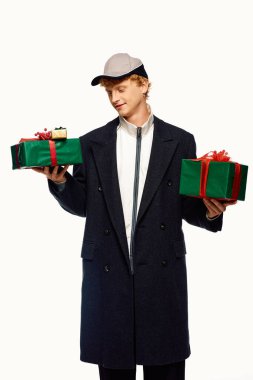 Bu şık adam iki güzel paketlenmiş Noel hediyesini neşeyle taşırken çağdaş tatil kıyafetlerini sergiliyor..