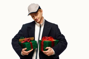 Modaya uygun bir adam 2025 Noel ruhunu kucaklıyor. Elinde canlı yaylarla süslenmiş hediyeler tutarken şık bir kıyafet sergiliyor..