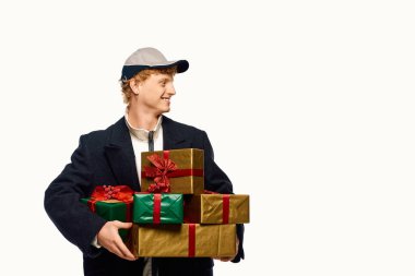 Moda kıyafetleri içinde neşeli bir adam, güzel paketlenmiş bir yığın Noel hediyesini taşırken gülümsüyor..