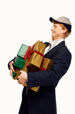 Genç bir adam güzel paketlenmiş Noel hediyelerini taşırken neşe saçar..