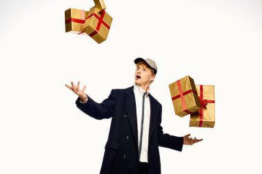 Şık bir adam güzel paketlenmiş Noel hediyeleriyle ustalıkla hokkabazlık yapar, neşeli bir pozla şenlik havası verir..