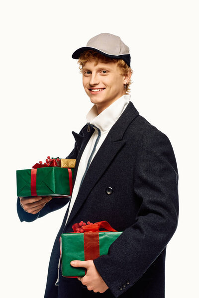 Нося модное зимнее пальто и кепку, молодой человек, держа в руках два красиво обернутых рождественских подарка.