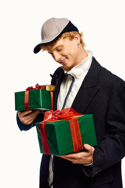 Стильный мужчина излучает праздничное настроение, держа праздничные зеленые подарочные коробки, украшенные красными лентами.